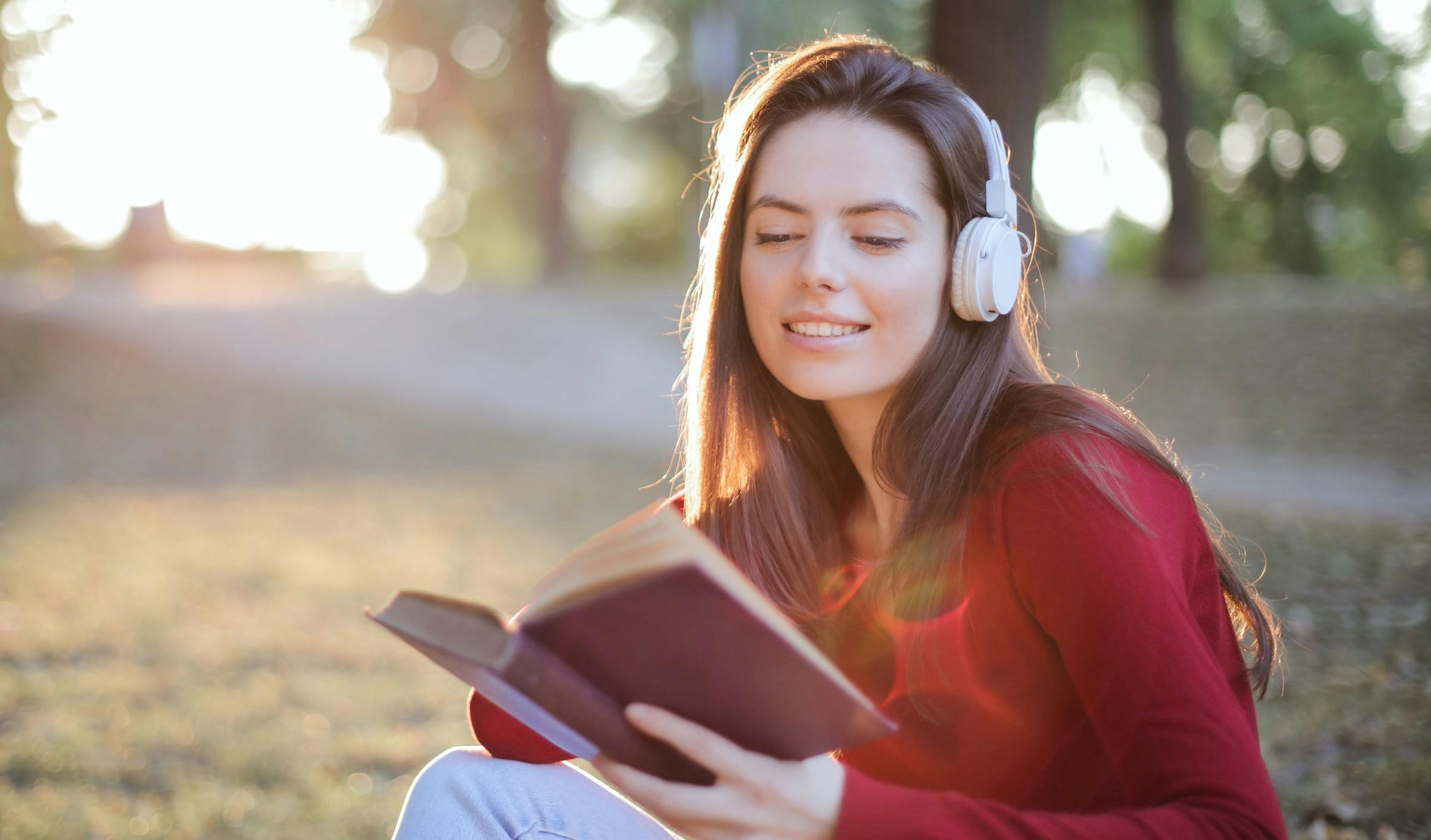 Young woman with headphones listening to music and reading a book.